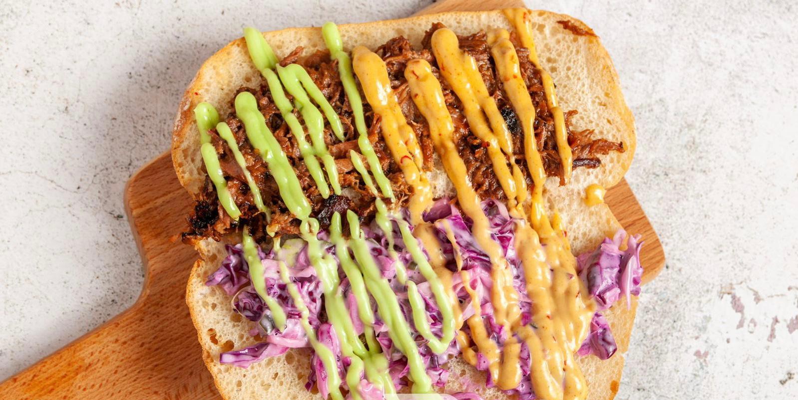 Long sandwich with grilled filling, slaw and green sauce drizzle